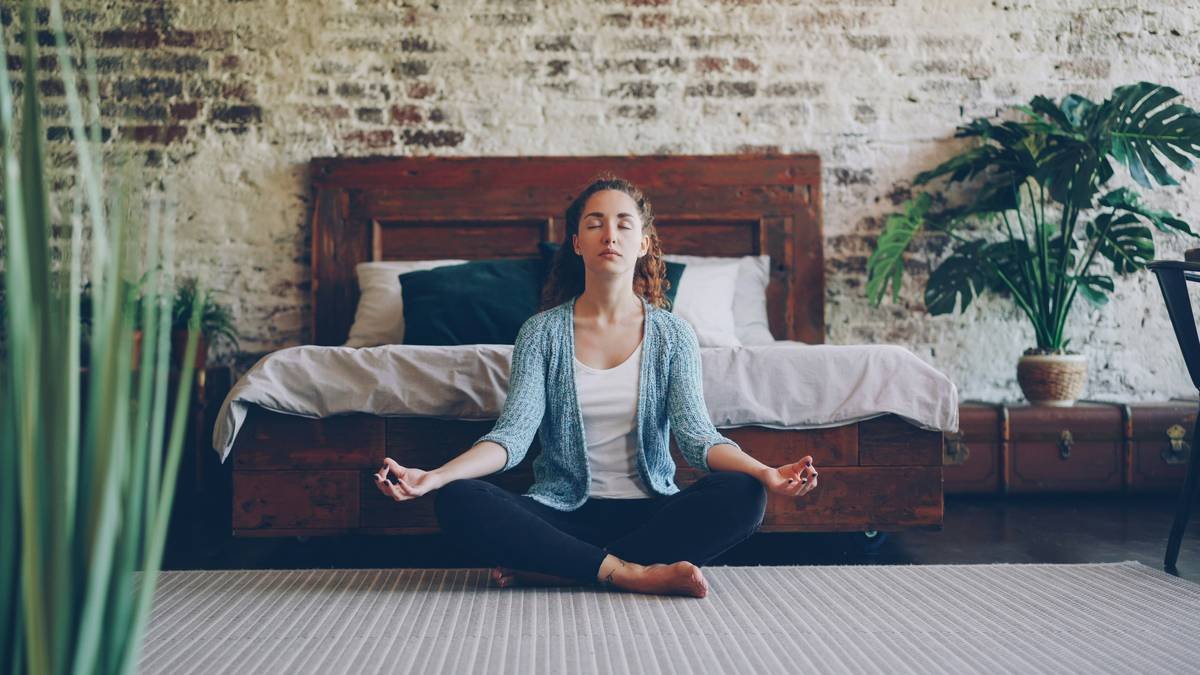 A serene woman meditating near a lake with mountains in the background